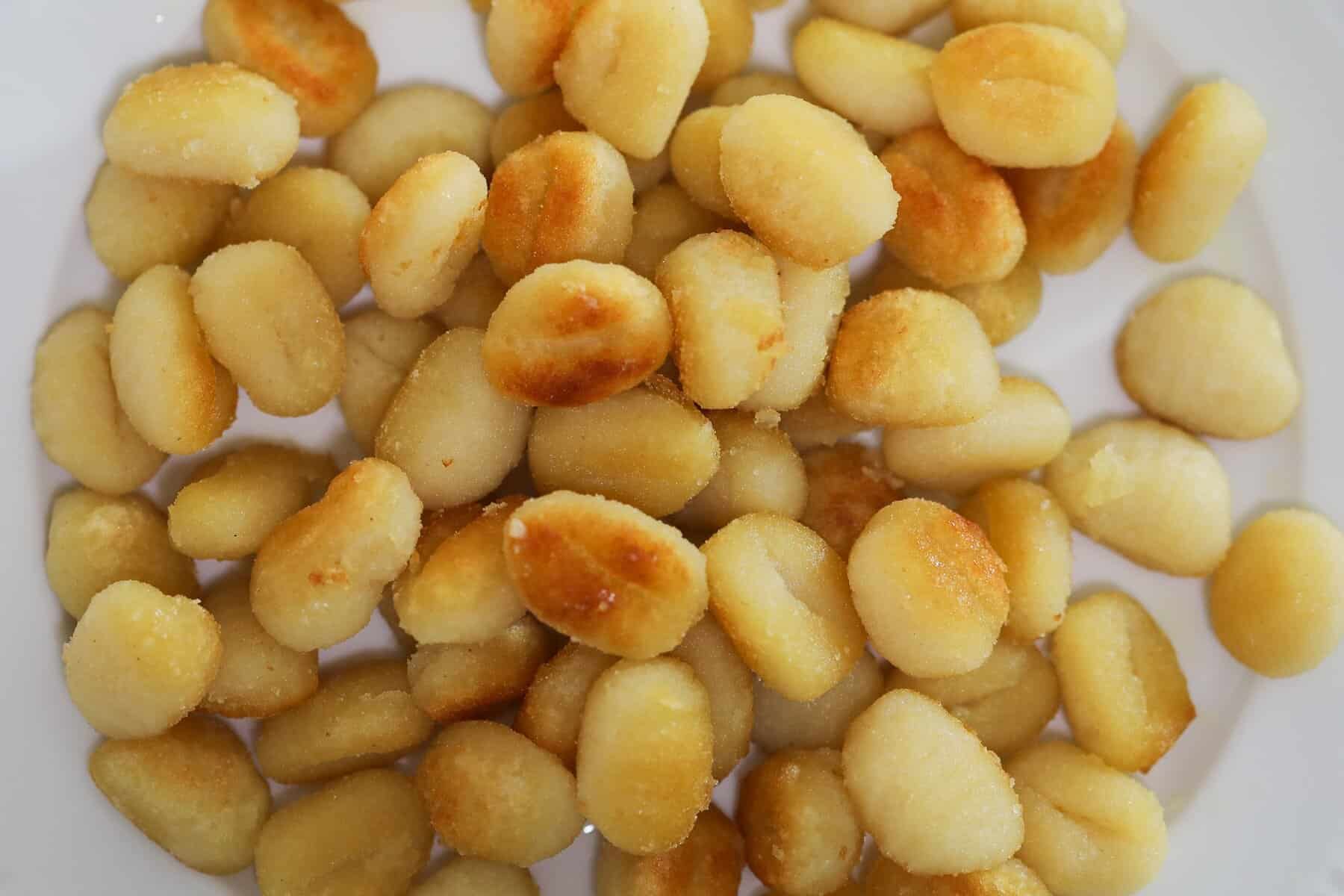 Shelf-stable gnocchi browning in olive oil in a skillet, crispy on one side for pan-fried gnocchi recipe